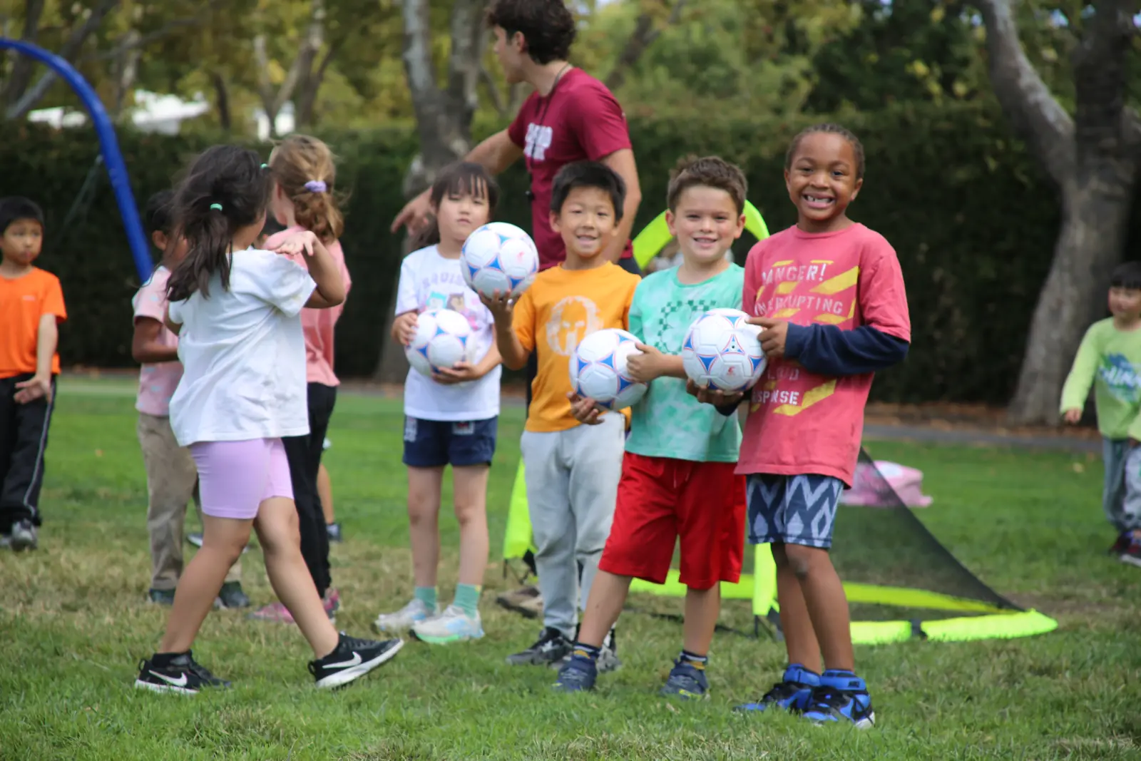 Smiling students holding soccer balls with their coach on a school field