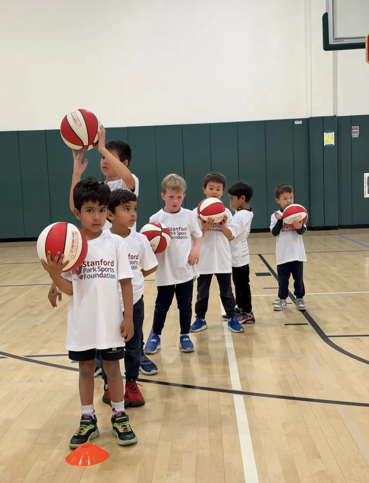 Young players lined up with basketballs in the gym