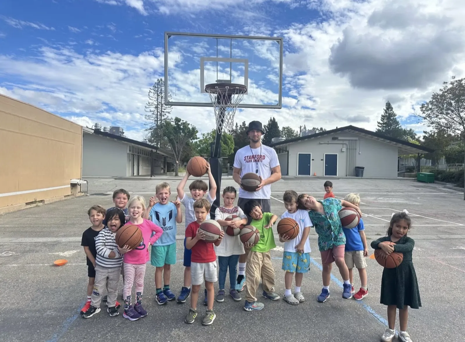 Students with basketballs and their coach on the school blacktop