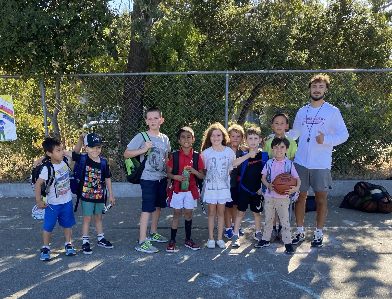 Coach with a group of smiling students after school by the fence